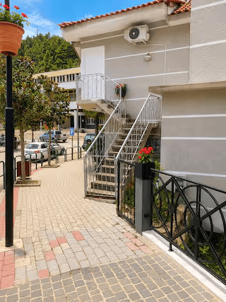 External view of a building with a metal staircase leading to a second floor, surrounded by trees and parked cars.