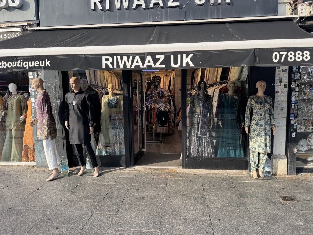 A storefront of 'Riwaaz UK' showcasing traditional clothing on mannequins outside, with various outfits displayed in the entrance area.